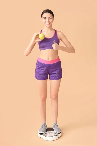 一个快乐的年轻女人 拿着苹果 站在有颜色背景的天平上 体重减轻概念 — 图库照片