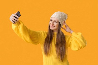 Kalın kazaklı güzel bir kadın arka planda selfie çekiyor.