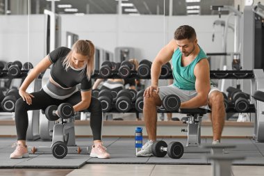 Spor salonunda dambıllarla spor yapan genç bir çift.