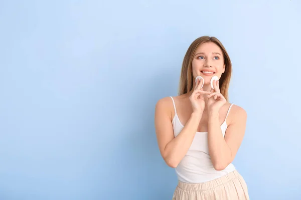 Beautiful young woman with cotton pads on color background