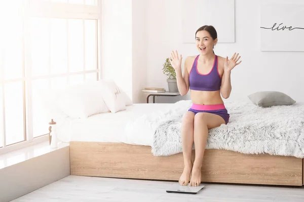 Happy young woman with weight scales at home