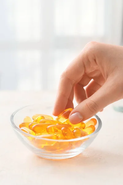Woman taking fish oil capsule from bowl on table