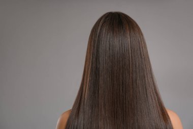 Gri arka planda güzel düz saçları olan genç bir kadın.