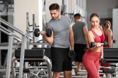 Spor salonunda dambıllarla spor yapan genç bir çift.