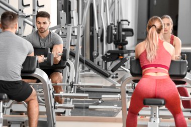 Spor salonunda dambıllarla spor yapan genç bir çift.