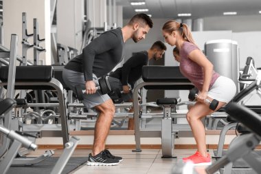 Spor salonunda dambıllarla spor yapan genç bir çift.