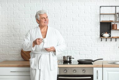 Olgun bir adam mutfakta kahve içiyor.