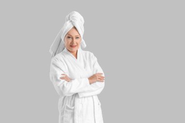 Gri arka planda bornoz giymiş olgun bir kadın.