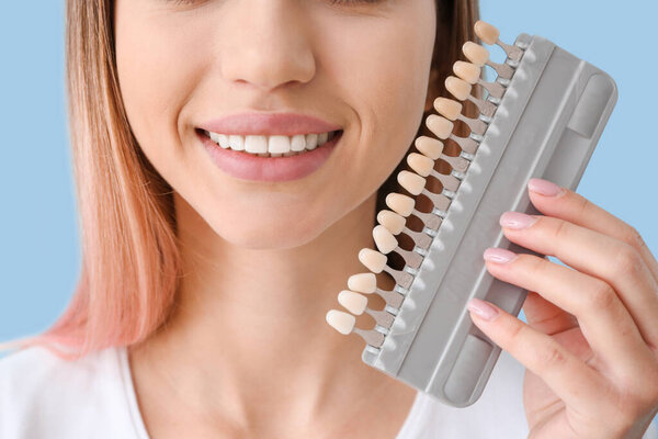 Beautiful young woman with teeth samples on color background, closeup