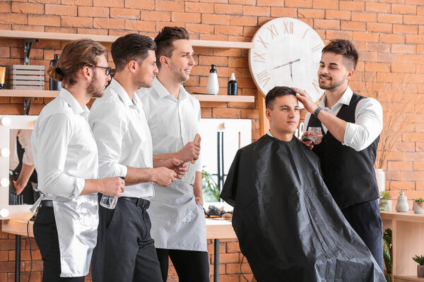 Professional hairdresser teaching young men in salon