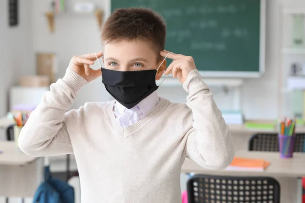 Little schoolboy in protective mask in classroom. Concept of epidemic