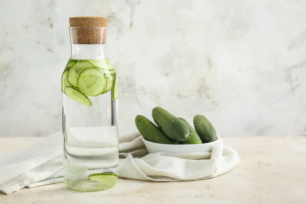 Bottle of infused cucumber water on light background