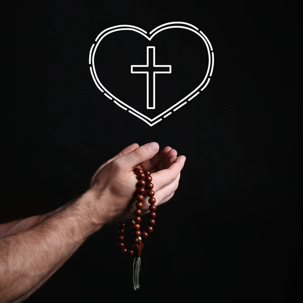 Male hands with rosary beads, cross and heart on black background