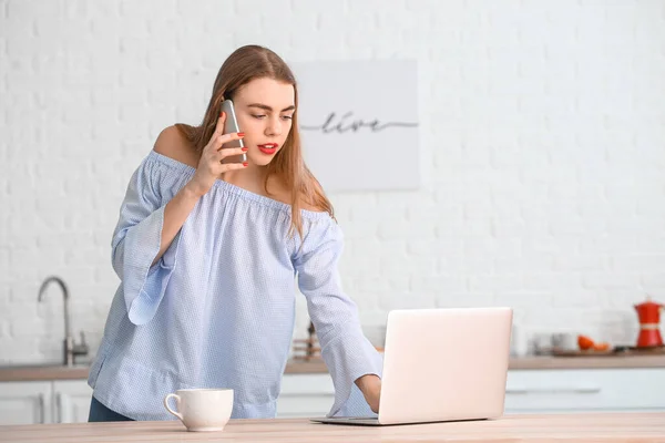 Bella Giovane Donna Che Parla Telefono Durante Utilizzo Laptop Cucina — Foto Stock