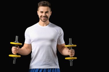 Koyu arkaplanda dambıllar olan sportif genç adam eğitimi.