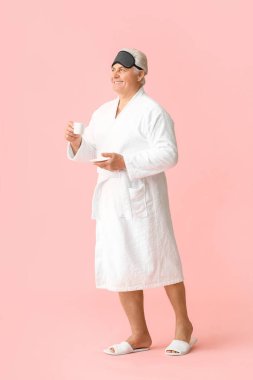 Bornozlu, mutlu, olgun bir adam. Uyku maskesi ve kahve rengi arka planda.