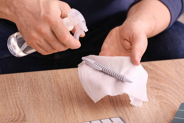 Man disinfecting his workplace in office, closeup