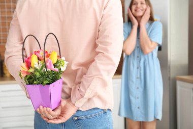 Evinde arkasında güzel bir kız arkadaş için çiçek tutan genç bir adam.