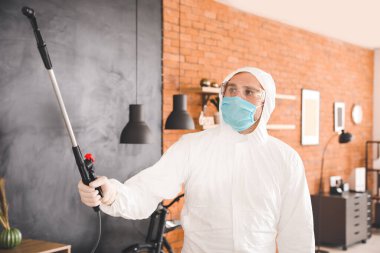 Biyolojik tehlike giysisi giyen bir işçi evi dezenfekte ediyor.