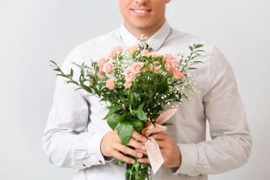 Açık arkaplanda çiçek demeti olan yakışıklı bir adam.