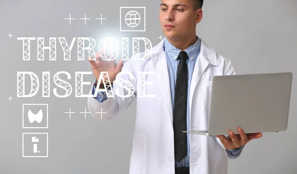Endocrinologist with laptop and text THYROID DISEASE on grey background