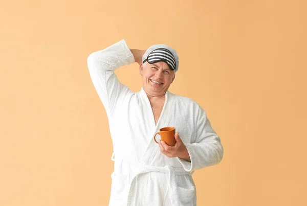 幸せな成熟した男でバスローブ 睡眠マスクと色の背景にコーヒーカップ — ストック写真