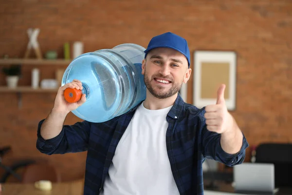Delivery man with bottle of water showing thumb-up in office