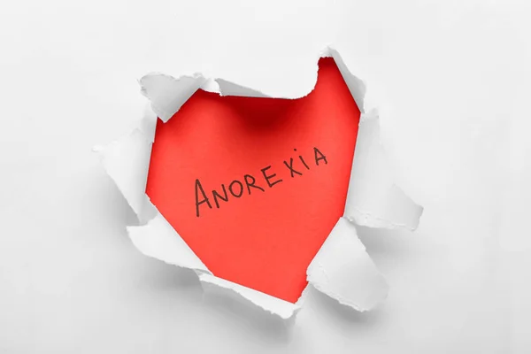 Word ANOREXIA visible through hole in torn paper