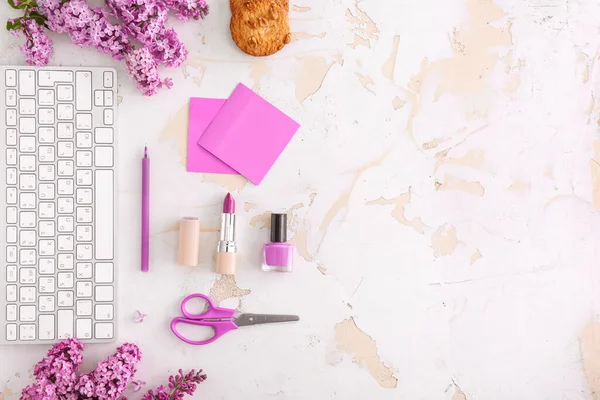 Beautiful lilac flowers, PC keyboard, stationery and cosmetics on table