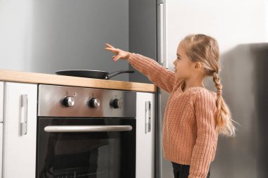 Evdeki elektrikli ocakta tavayla oynayan küçük bir kız.