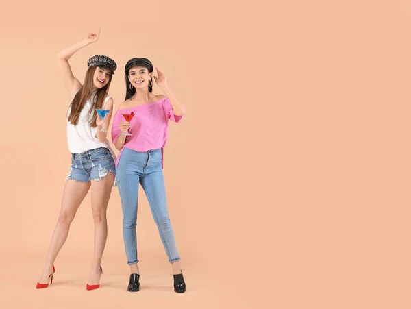 Happy young women with cocktails on color background