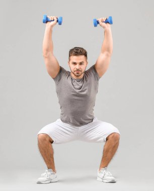 Gri arka planda dambılları olan sportif genç adam eğitimi.