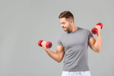 Gri arka planda dambılları olan sportif genç adam eğitimi.