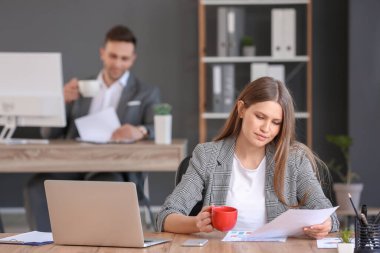 Ofiste çalışırken kahve içen genç bir kadın.