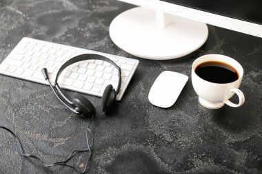 Kulaklık, bilgisayar ve kahve ofisteki teknik destek ajanının masasında.