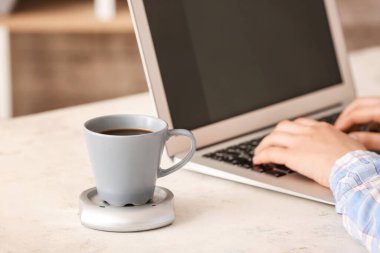 Laptopla çalışan bir kadının masasında ısıtıcısı olan bir fincan kahve.