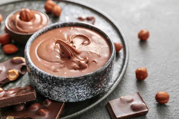 Bowl with tasty chocolate paste and hazelnuts on grey background