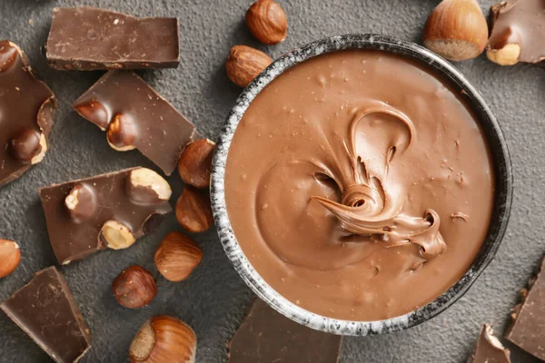 Bowl with tasty chocolate paste and hazelnuts on grey background