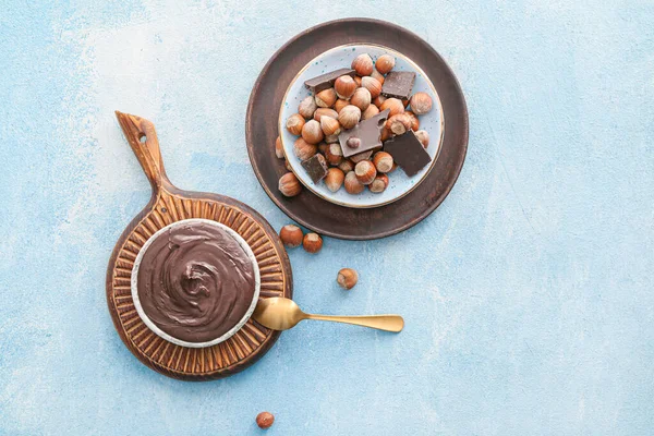 Plates with tasty chocolate paste and hazelnuts on color background
