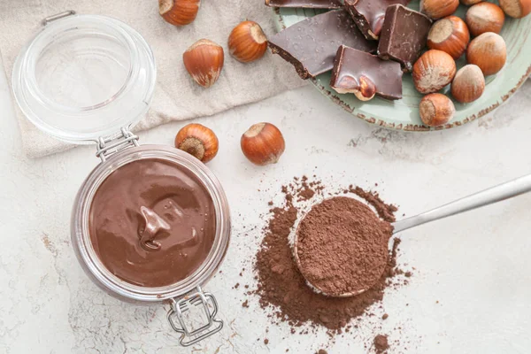 Jar with tasty chocolate paste and hazelnuts on light background