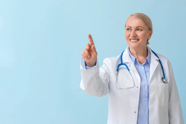 Reife Ärztin Zeigt Auf Etwas Auf Farbigem Hintergrund — Stockfoto