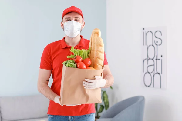 Male courier of food delivery company in medical mask indoors