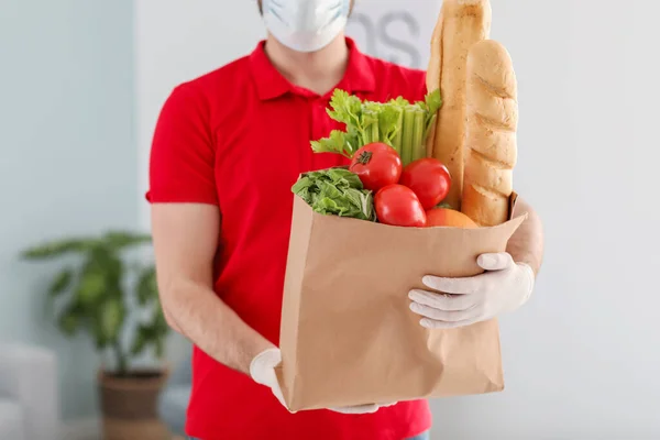 Male courier of food delivery company in medical mask indoors