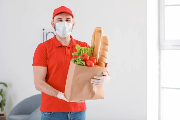 Male courier of food delivery company in medical mask indoors