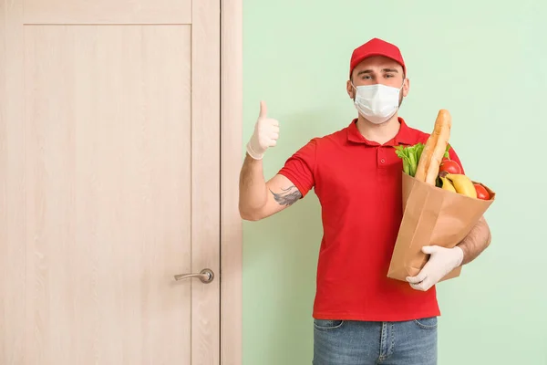 Male courier of food delivery company in medical mask near customer\'s door