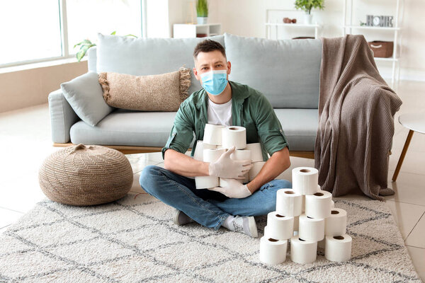 Man in mask and with heap of toilet paper at home. Concept of coronavirus epidemic