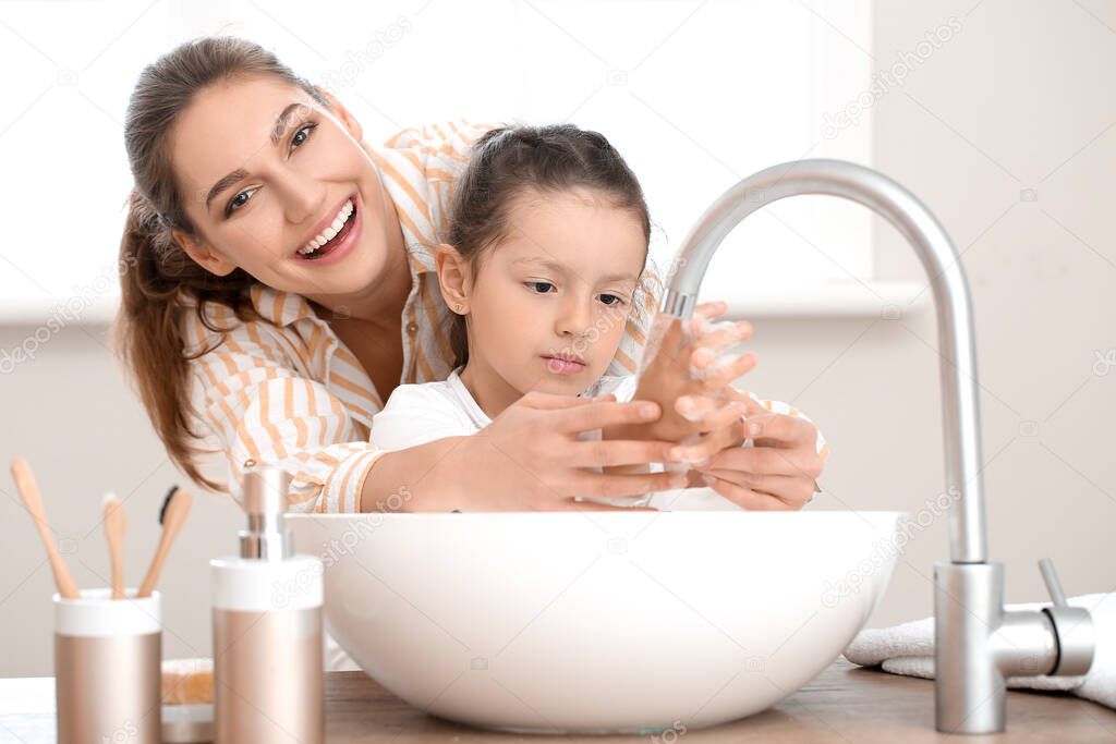 Little daughter with her mother washing hands in bathroom