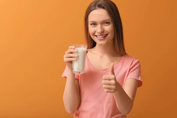 拿着一杯牛奶的年轻女人在彩色背景上表现出大拇指向上的姿势 — 图库照片