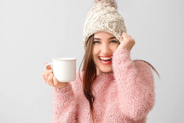 Beautiful happy young woman with cup of hot cocoa on light background