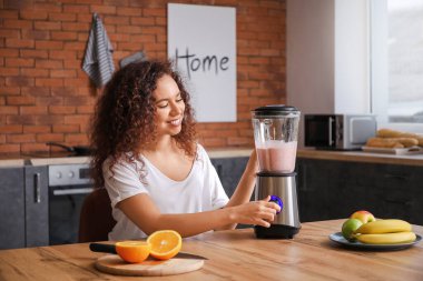 Genç bir kadın mutfakta smoothie yapıyor.